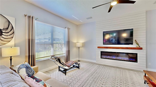 living room with ceiling fan, a textured ceiling, a fireplace, and light hardwood / wood-style floors