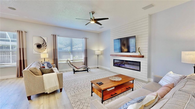 living room with ceiling fan, a fireplace, a textured ceiling, and light wood-type flooring