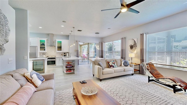 living room featuring wine cooler, sink, a textured ceiling, light wood-type flooring, and ceiling fan