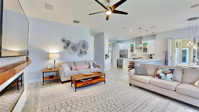 living room with sink, ceiling fan with notable chandelier, a fireplace, and light hardwood / wood-style floors