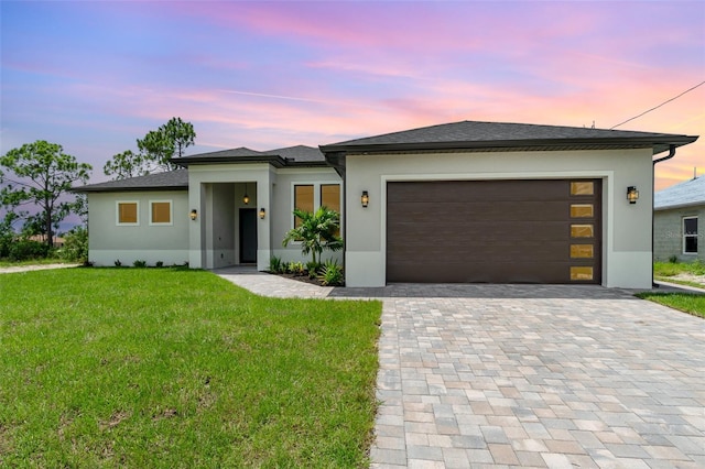 prairie-style home featuring a garage, a yard, decorative driveway, and stucco siding