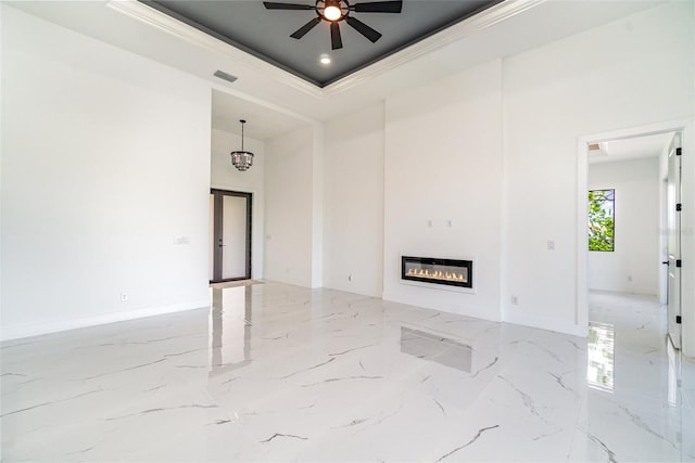 unfurnished living room with a tray ceiling, marble finish floor, visible vents, ornamental molding, and a glass covered fireplace