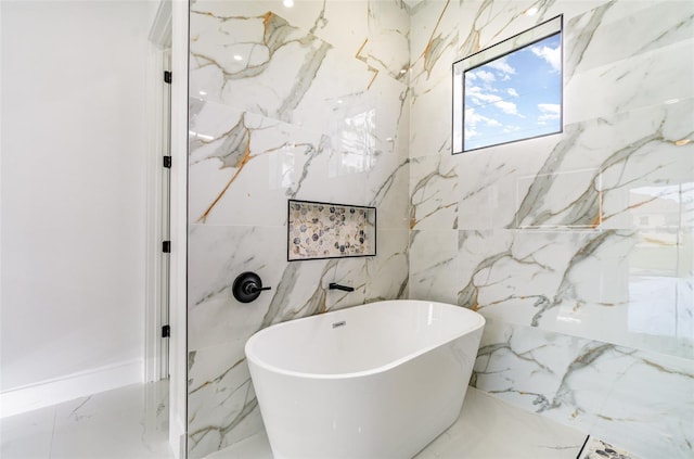 full bath with a freestanding tub, marble finish floor, and stone wall