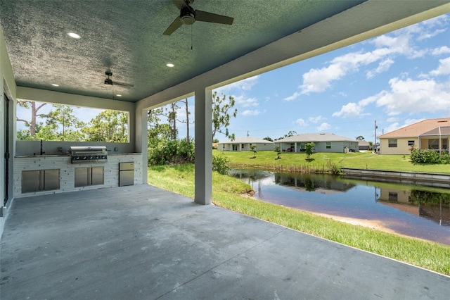 view of patio with a grill, a water view, an outdoor kitchen, and ceiling fan