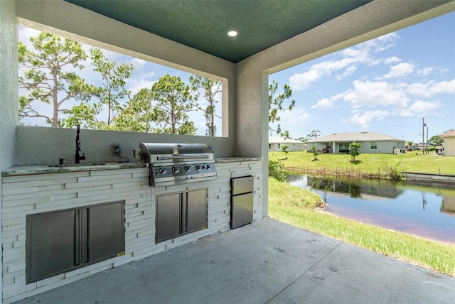 view of patio / terrace with a water view, exterior kitchen, sink, and a grill