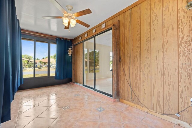 tiled empty room featuring wooden walls and ceiling fan