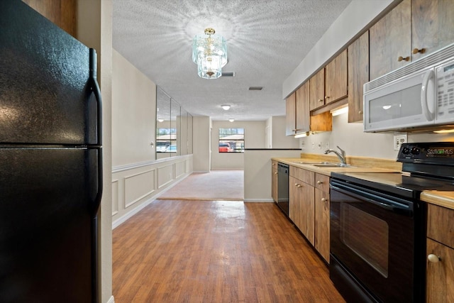 kitchen with light hardwood / wood-style flooring, black appliances, sink, a textured ceiling, and a chandelier