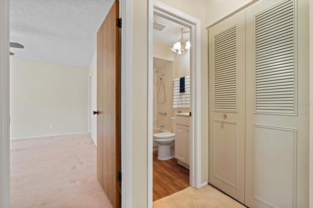 hallway with light carpet, a notable chandelier, and a textured ceiling