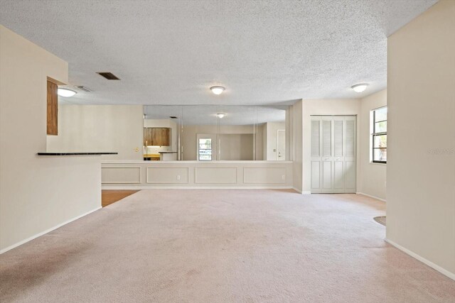 unfurnished living room featuring a textured ceiling and light colored carpet