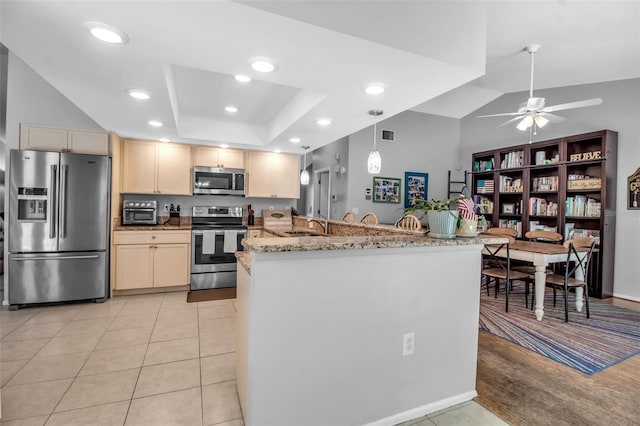 kitchen featuring appliances with stainless steel finishes, hanging light fixtures, a tray ceiling, light stone countertops, and kitchen peninsula