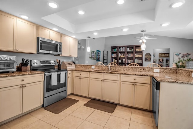 kitchen with appliances with stainless steel finishes, a tray ceiling, cream cabinets, and kitchen peninsula