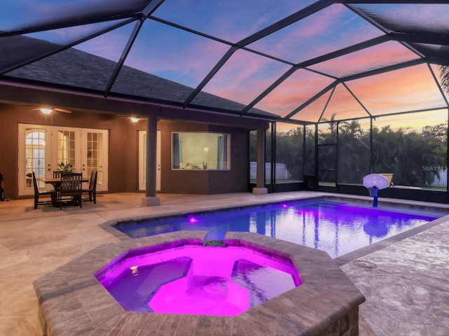 pool at dusk with glass enclosure, ceiling fan, french doors, a patio area, and an in ground hot tub