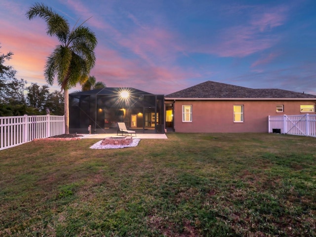 back house at dusk featuring a yard, glass enclosure, and a patio area