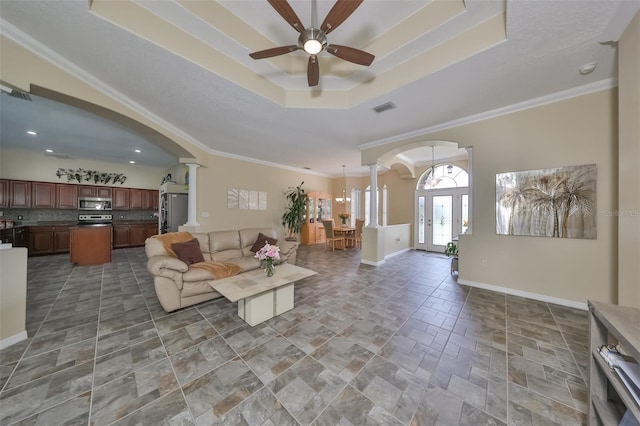living room featuring ornate columns, a raised ceiling, visible vents, a ceiling fan, and arched walkways