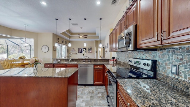 kitchen with backsplash, a sink, stone finish flooring, a peninsula, and appliances with stainless steel finishes