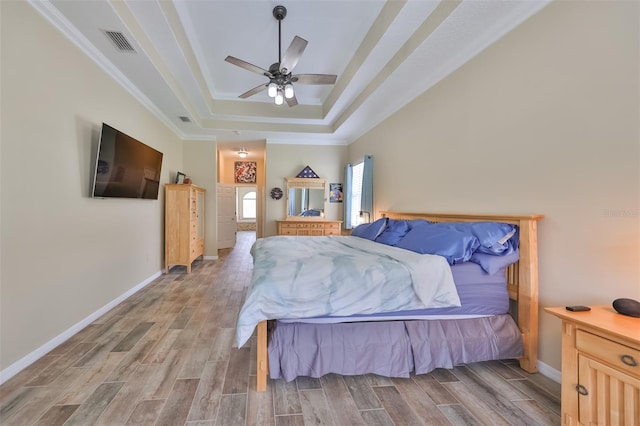bedroom featuring visible vents, baseboards, wood finished floors, and a tray ceiling