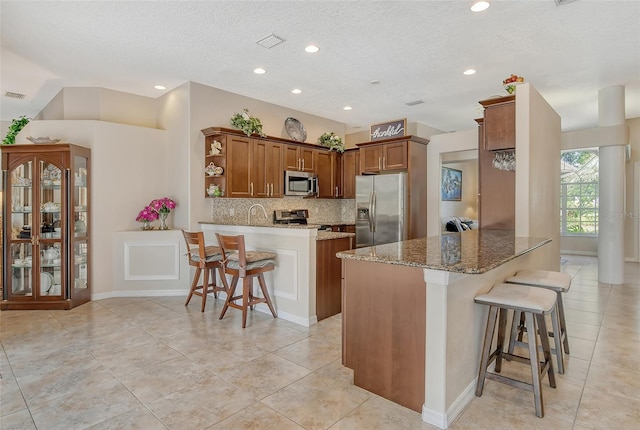 kitchen featuring a kitchen bar, stone counters, stainless steel appliances, kitchen peninsula, and light tile patterned floors