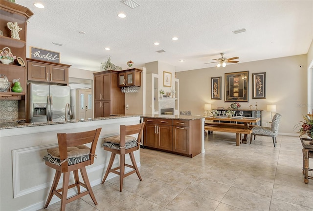 kitchen featuring stainless steel fridge, light stone counters, light tile patterned floors, and ceiling fan