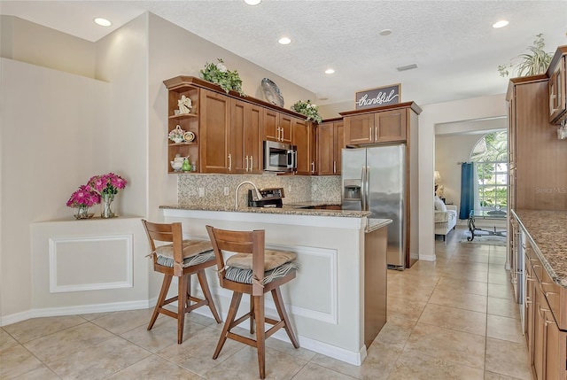 kitchen with light tile patterned floors, kitchen peninsula, backsplash, light stone countertops, and appliances with stainless steel finishes