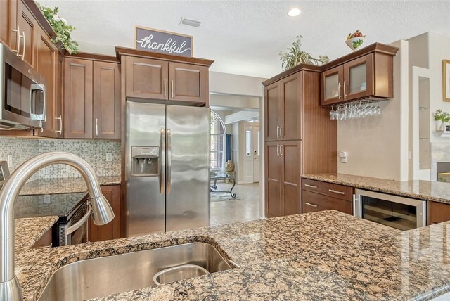 kitchen featuring beverage cooler, stone counters, appliances with stainless steel finishes, a textured ceiling, and backsplash