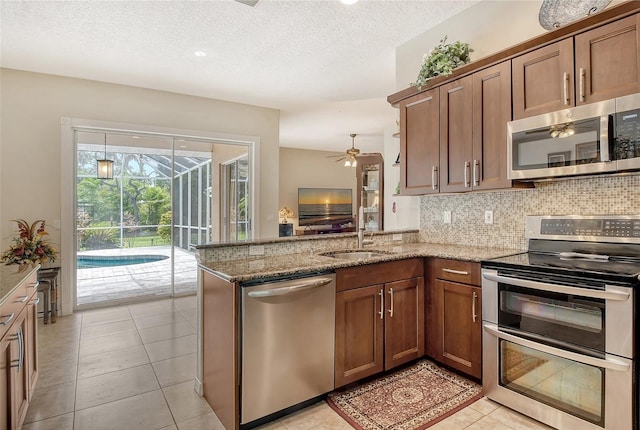 kitchen featuring ceiling fan, stainless steel appliances, light stone counters, and kitchen peninsula