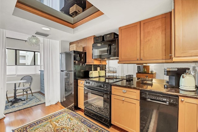 kitchen with a tray ceiling, dark stone counters, black appliances, and light hardwood / wood-style floors