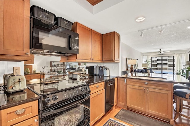 kitchen with black appliances, sink, rail lighting, ceiling fan, and kitchen peninsula