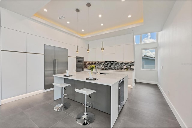 kitchen featuring stainless steel appliances, a tray ceiling, a center island with sink, and backsplash