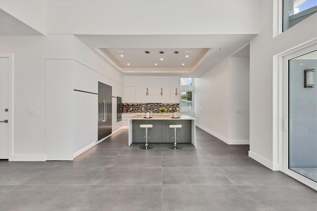 kitchen featuring an island with sink, a tray ceiling, a kitchen bar, and white cabinetry