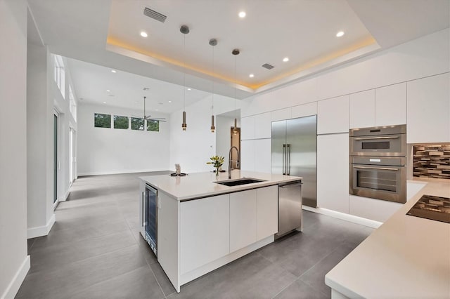 kitchen with pendant lighting, an island with sink, sink, white cabinetry, and a tray ceiling