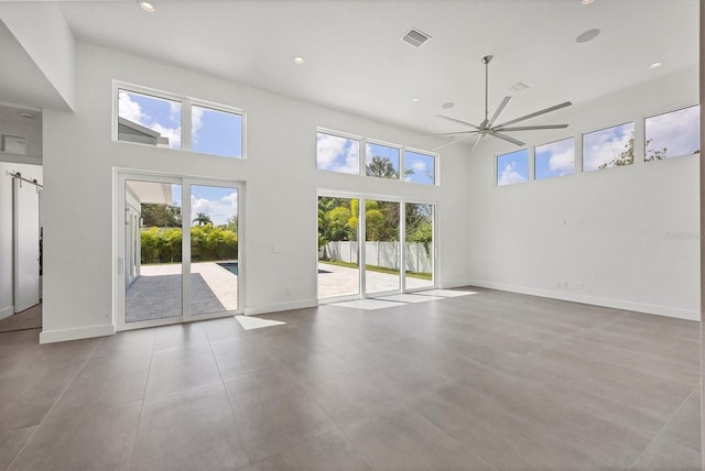 unfurnished room featuring ceiling fan, a towering ceiling, and a barn door