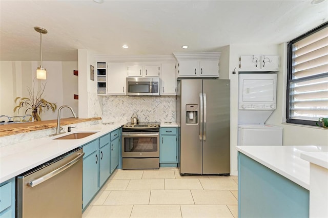 kitchen featuring pendant lighting, sink, stainless steel appliances, stacked washer / drying machine, and white cabinets