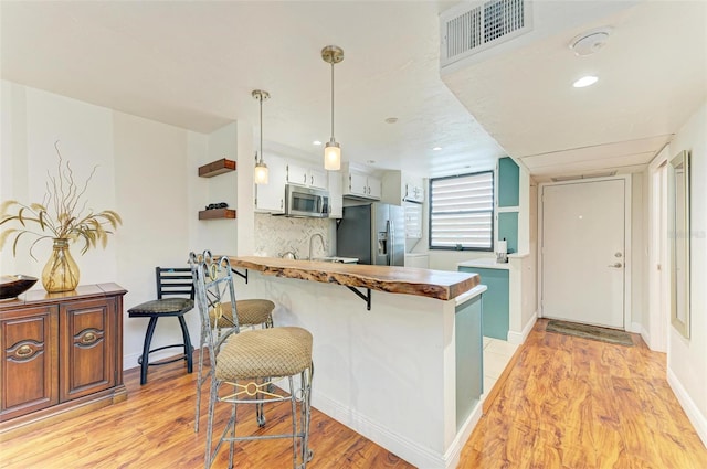 kitchen featuring a breakfast bar area, white cabinetry, hanging light fixtures, kitchen peninsula, and stainless steel appliances