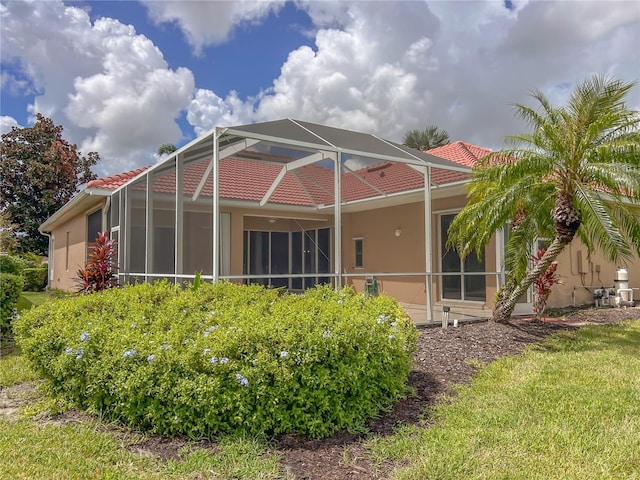 rear view of house featuring glass enclosure, a tile roof, and stucco siding