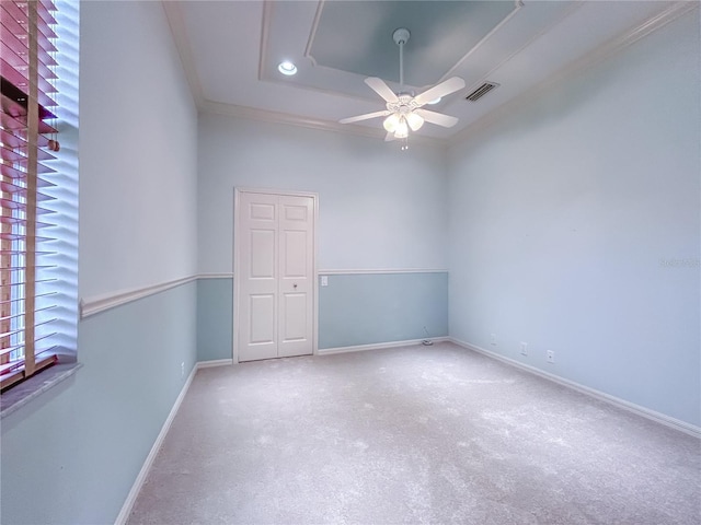 spare room with baseboards, visible vents, a ceiling fan, a tray ceiling, and crown molding