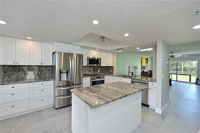 kitchen with tasteful backsplash, a kitchen island, appliances with stainless steel finishes, light stone countertops, and a sink