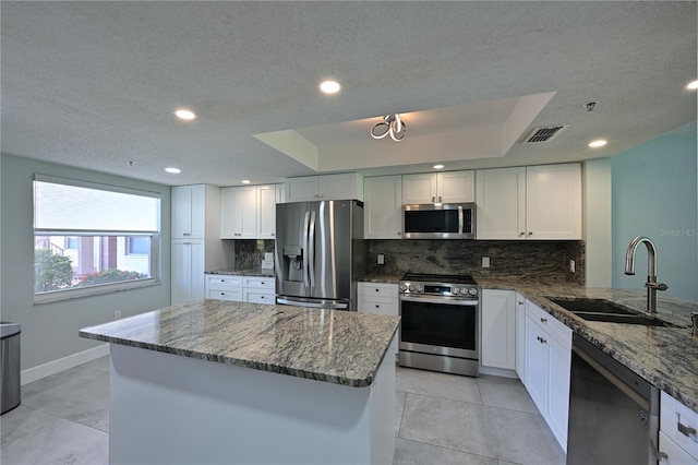 kitchen with tasteful backsplash, appliances with stainless steel finishes, white cabinets, a sink, and dark stone counters