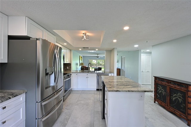 kitchen with stainless steel appliances, white cabinets, a sink, a kitchen island, and light stone countertops