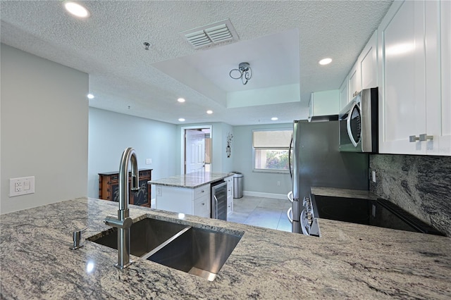 kitchen featuring light stone counters, range with electric stovetop, stainless steel microwave, visible vents, and a sink