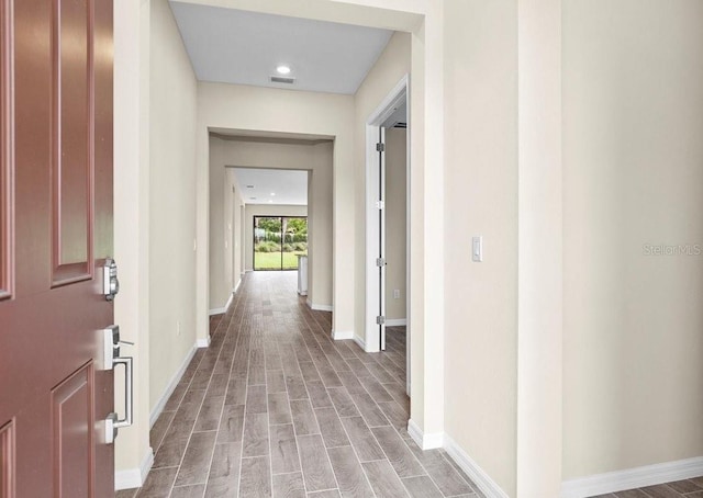 hall featuring visible vents, baseboards, and wood finished floors