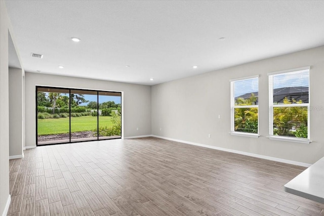 empty room with a wealth of natural light, visible vents, light wood-style flooring, and baseboards