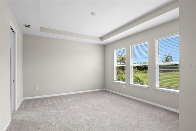 unfurnished room with a tray ceiling, visible vents, light carpet, and baseboards