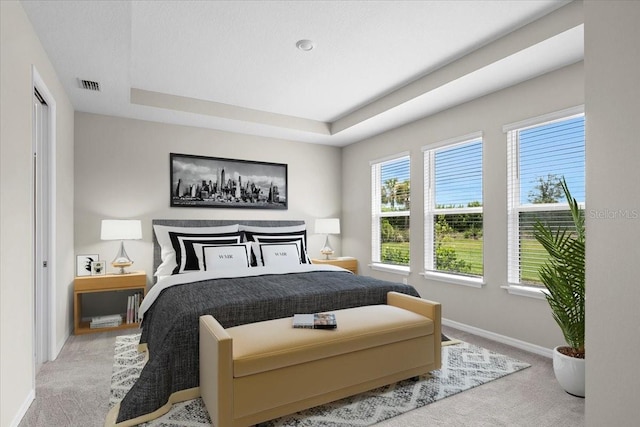 bedroom featuring light carpet, baseboards, visible vents, and a tray ceiling