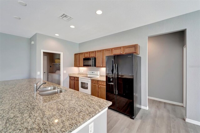 kitchen featuring washing machine and clothes dryer, light wood-type flooring, black appliances, and sink