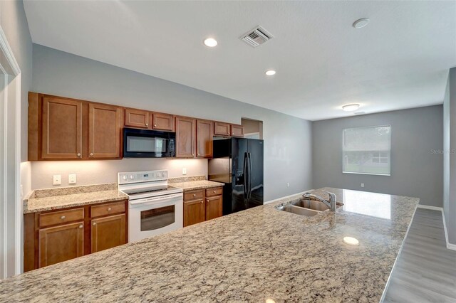 kitchen featuring light hardwood / wood-style floors, sink, black appliances, and light stone countertops