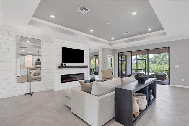 tiled living room featuring a fireplace, crown molding, and a tray ceiling