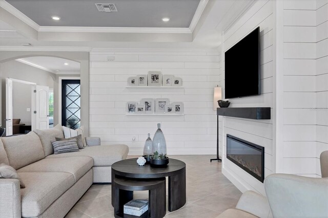 living room with light tile patterned flooring, a raised ceiling, and ornamental molding