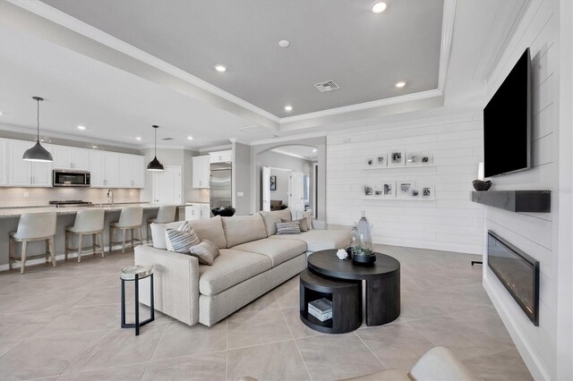 tiled living room featuring sink, crown molding, and a raised ceiling