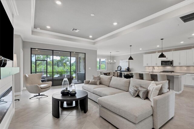 living room featuring light tile patterned flooring, a notable chandelier, crown molding, and a tray ceiling