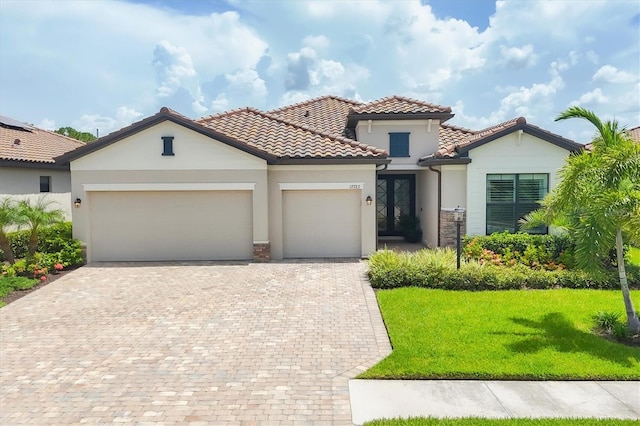 mediterranean / spanish house with an attached garage, a tile roof, decorative driveway, stucco siding, and a front yard